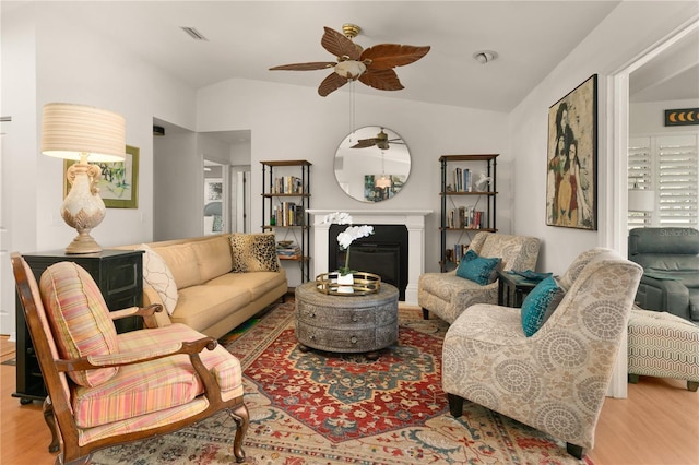 living area featuring visible vents, lofted ceiling, a glass covered fireplace, and wood finished floors