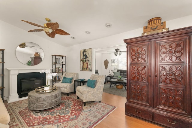 living room featuring ceiling fan, lofted ceiling, a glass covered fireplace, and light wood finished floors