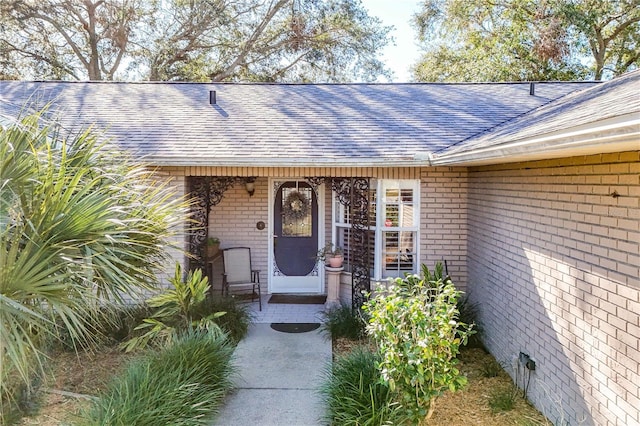 property entrance with a shingled roof and brick siding