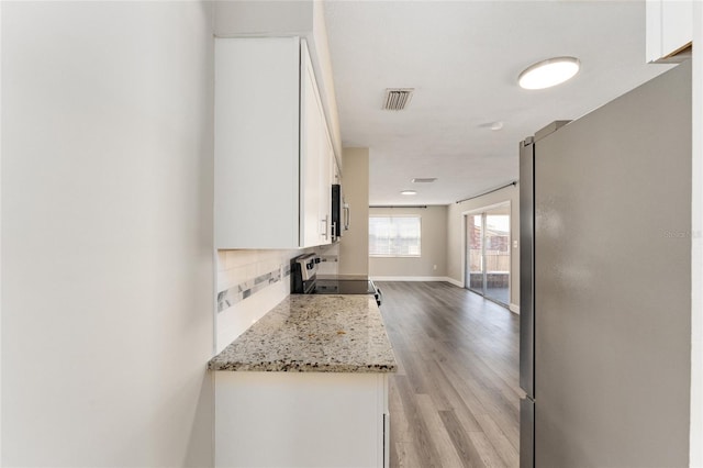 kitchen with light stone countertops, backsplash, range, white cabinetry, and stainless steel refrigerator