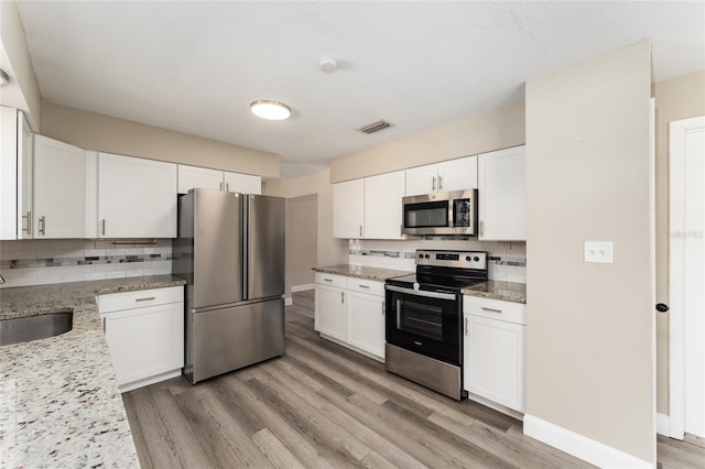 kitchen with white cabinetry, light stone countertops, sink, decorative backsplash, and appliances with stainless steel finishes