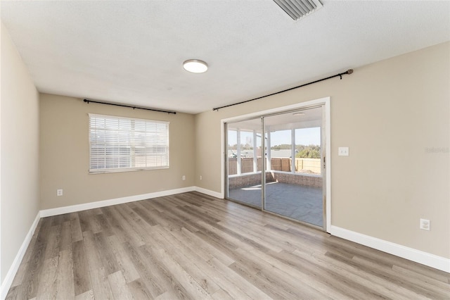 spare room featuring a textured ceiling, light hardwood / wood-style floors, and a healthy amount of sunlight