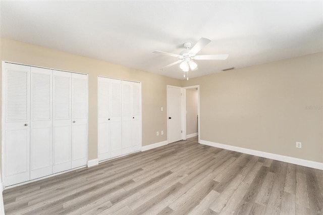 unfurnished bedroom with ceiling fan, light hardwood / wood-style flooring, and two closets