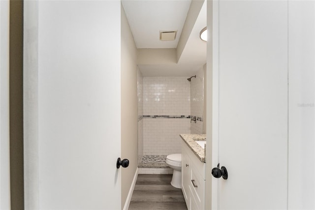 bathroom featuring tiled shower, hardwood / wood-style floors, vanity, and toilet