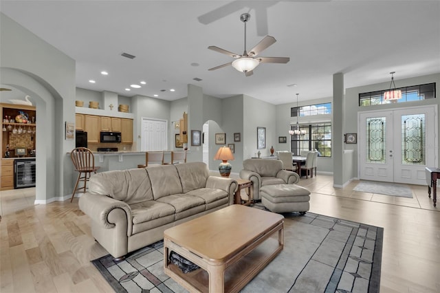 living room with a high ceiling, beverage cooler, ceiling fan with notable chandelier, and light wood-type flooring