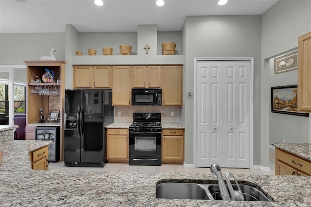 kitchen with beverage cooler, light brown cabinets, light stone countertops, a sink, and black appliances