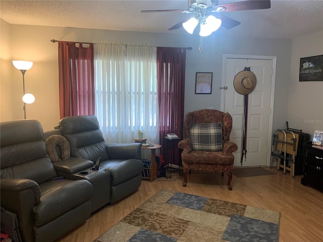 living room featuring ceiling fan, light hardwood / wood-style flooring, and a textured ceiling