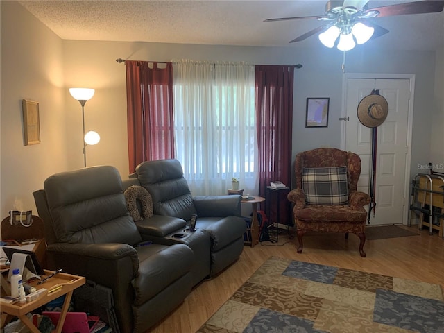 living room with ceiling fan, a textured ceiling, and light wood-type flooring