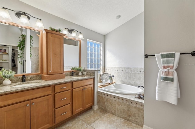 bathroom with vaulted ceiling, a textured ceiling, vanity, tiled tub, and tile patterned flooring