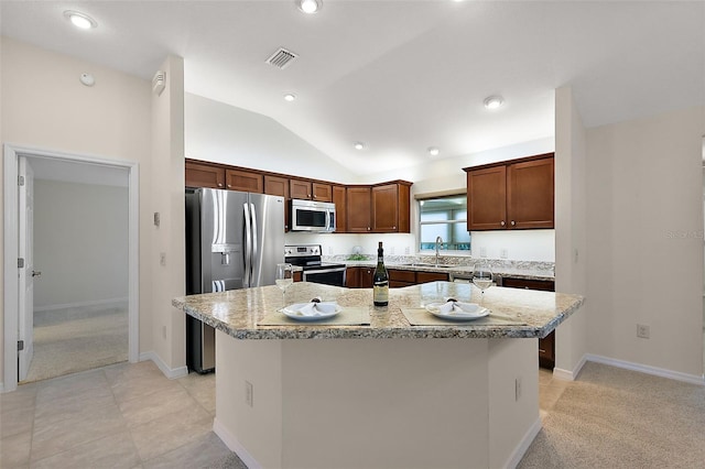 kitchen featuring light stone counters, a kitchen island, lofted ceiling, appliances with stainless steel finishes, and sink