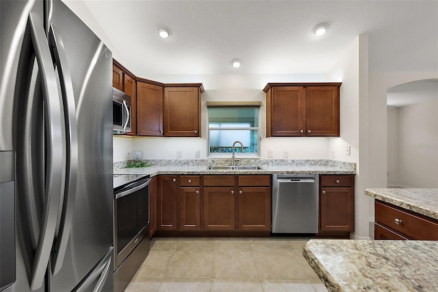 kitchen featuring appliances with stainless steel finishes, light stone countertops, sink, and light tile patterned floors