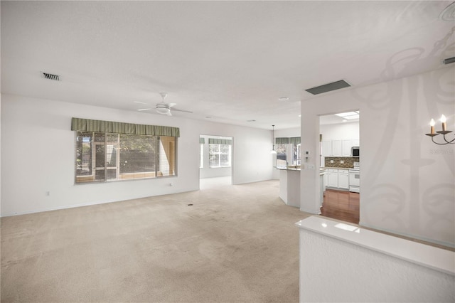 unfurnished living room featuring ceiling fan with notable chandelier and light colored carpet