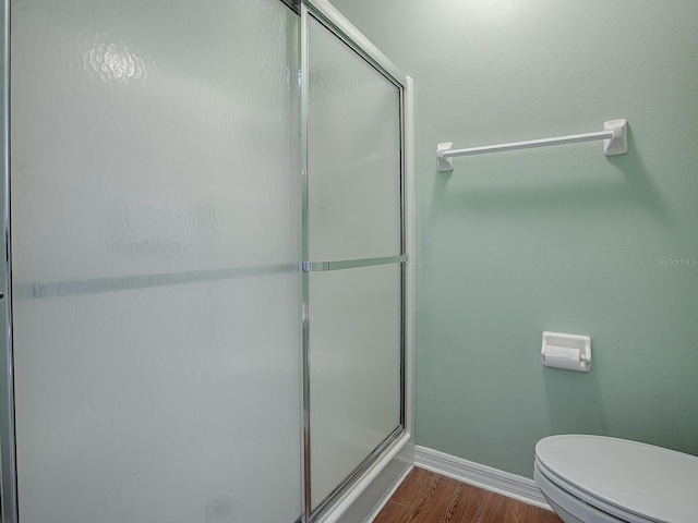 bathroom featuring toilet, a shower with shower door, and wood-type flooring