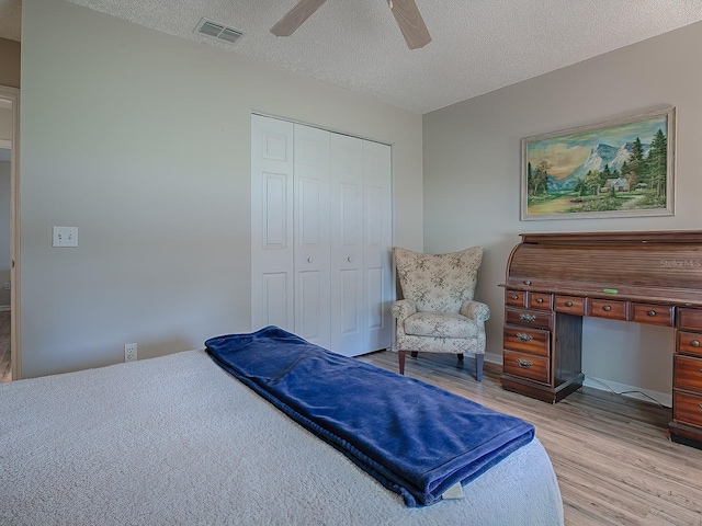 bedroom with a textured ceiling, a closet, light hardwood / wood-style flooring, and ceiling fan