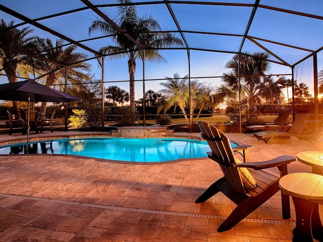 pool at dusk with glass enclosure and a patio area