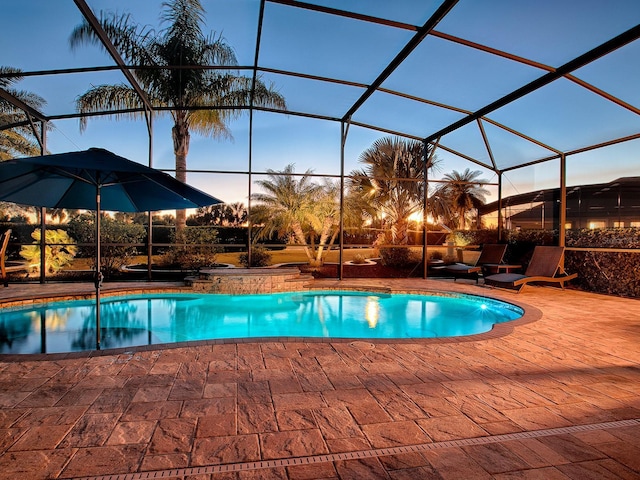 pool at dusk featuring glass enclosure and a patio area