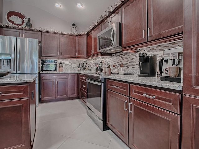 kitchen with light stone countertops, decorative backsplash, stainless steel appliances, light tile patterned floors, and lofted ceiling