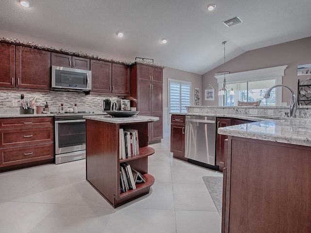 kitchen featuring hanging light fixtures, vaulted ceiling, light stone countertops, a kitchen island, and stainless steel appliances