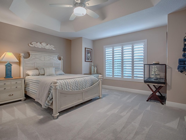 bedroom with light colored carpet, a raised ceiling, and ceiling fan