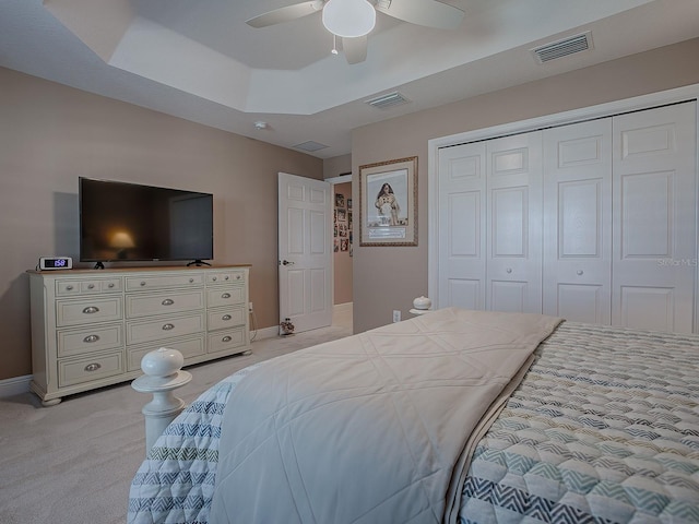 bedroom featuring a raised ceiling, ceiling fan, a closet, and light colored carpet