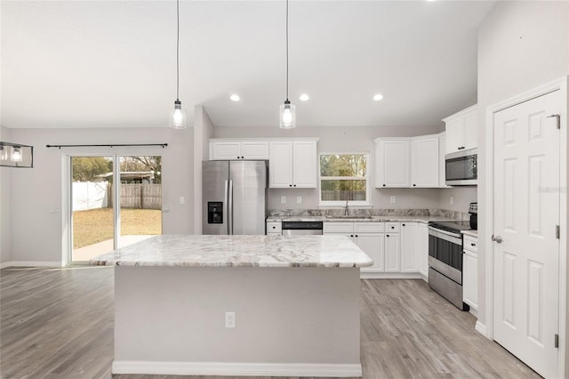 kitchen with a center island, hanging light fixtures, appliances with stainless steel finishes, light stone counters, and white cabinetry