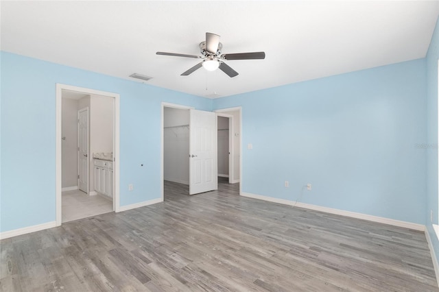 unfurnished bedroom with light hardwood / wood-style flooring, ceiling fan, a spacious closet, connected bathroom, and a closet