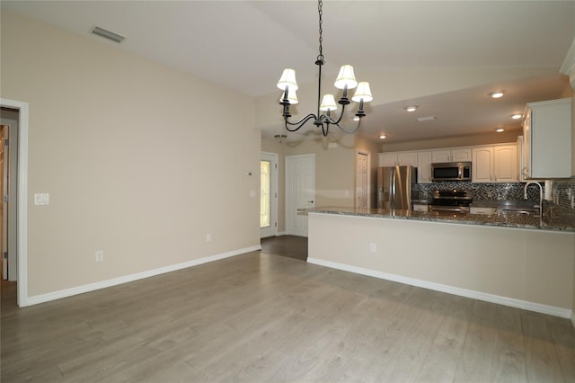 kitchen featuring pendant lighting, sink, dark stone countertops, kitchen peninsula, and stainless steel appliances