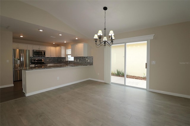 kitchen with kitchen peninsula, stainless steel appliances, vaulted ceiling, white cabinetry, and hanging light fixtures