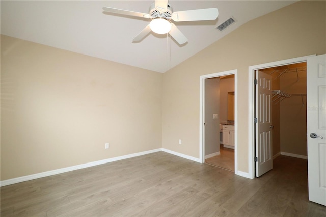 unfurnished bedroom with light wood-type flooring, vaulted ceiling, ceiling fan, a spacious closet, and a closet