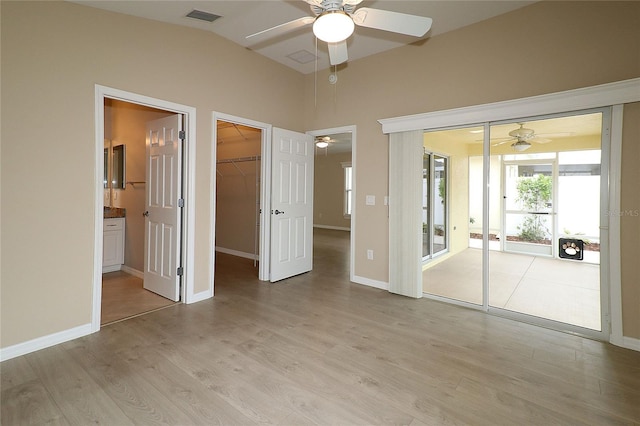 unfurnished bedroom featuring ceiling fan, a spacious closet, ensuite bathroom, vaulted ceiling, and light wood-type flooring