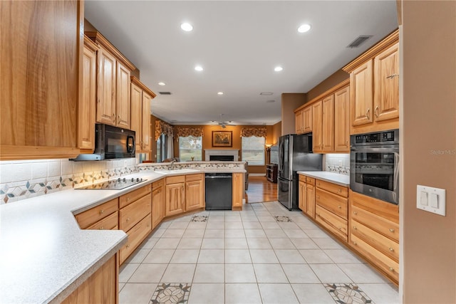 kitchen featuring kitchen peninsula, decorative backsplash, light tile patterned flooring, black appliances, and sink