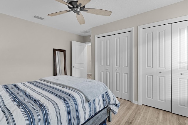 bedroom with light hardwood / wood-style flooring, ceiling fan, and multiple closets