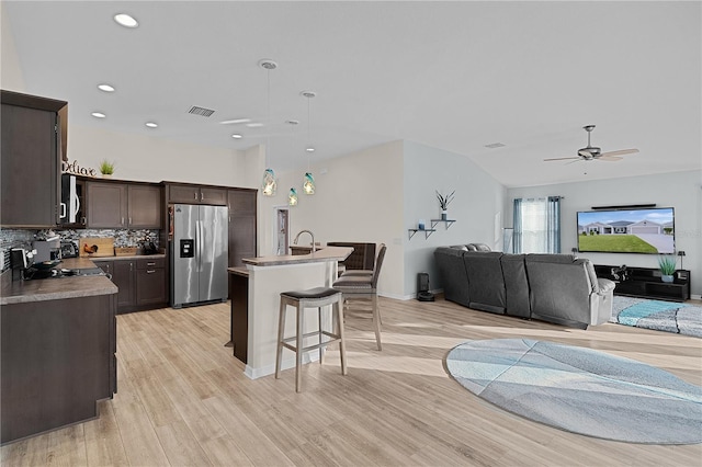 kitchen with stainless steel fridge, dark brown cabinets, a center island with sink, and hanging light fixtures