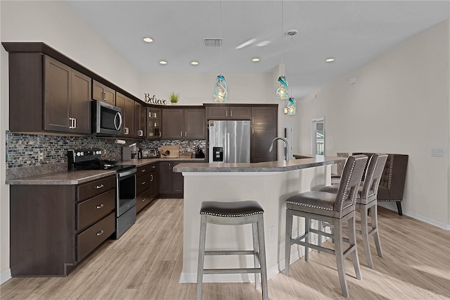 kitchen featuring pendant lighting, a center island with sink, light hardwood / wood-style flooring, dark brown cabinets, and stainless steel appliances