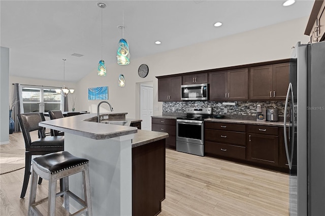 kitchen with sink, stainless steel appliances, a kitchen breakfast bar, decorative light fixtures, and a center island with sink