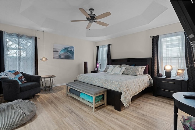 bedroom featuring a raised ceiling, multiple windows, ceiling fan, and light hardwood / wood-style flooring