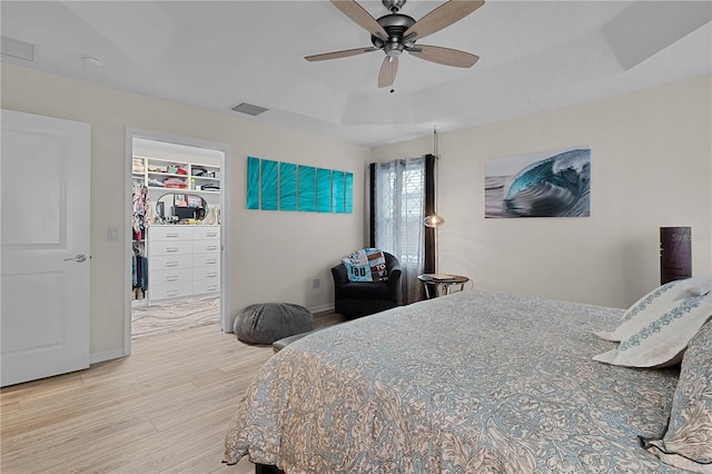 bedroom with a spacious closet, ceiling fan, a tray ceiling, a closet, and light wood-type flooring