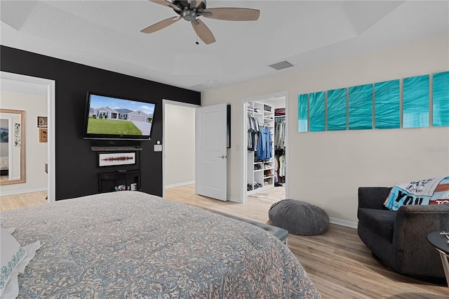 bedroom featuring ceiling fan, a spacious closet, wood-type flooring, a tray ceiling, and a closet