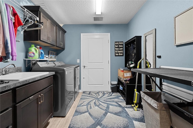 laundry room featuring washing machine and dryer, sink, cabinets, and a textured ceiling