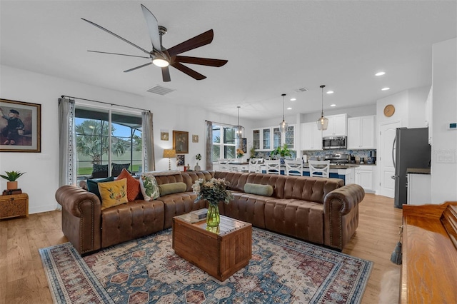 living room with light wood-type flooring, ceiling fan, and a healthy amount of sunlight