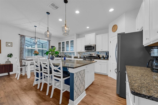 kitchen featuring a center island, a breakfast bar, white cabinets, dark stone counters, and appliances with stainless steel finishes