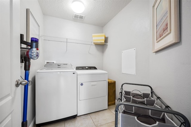 laundry area featuring a textured ceiling, washing machine and dryer, and light tile patterned flooring