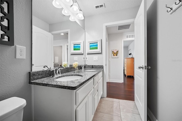 bathroom with a textured ceiling, tile patterned flooring, vanity, and toilet