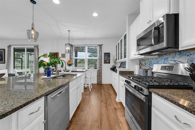 kitchen featuring hanging light fixtures, stainless steel appliances, white cabinets, dark stone countertops, and sink