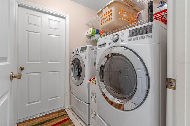 clothes washing area featuring light tile patterned flooring, a textured ceiling, and washing machine and clothes dryer