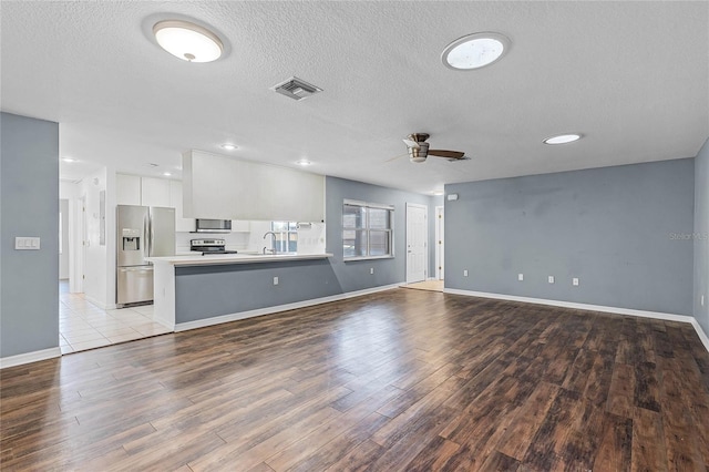 unfurnished living room featuring a textured ceiling, ceiling fan, light wood-type flooring, and sink