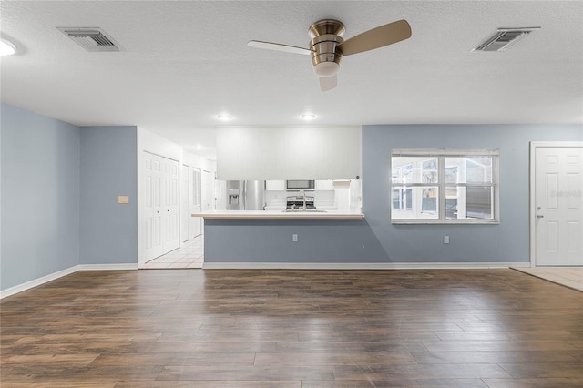 unfurnished living room with a textured ceiling, ceiling fan, and dark hardwood / wood-style floors