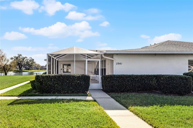 view of front of house featuring a lanai, a water view, and a front lawn