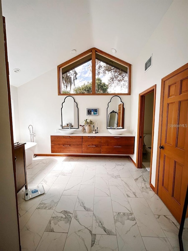 bathroom with a washtub, vanity, vaulted ceiling, and toilet