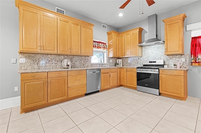 kitchen featuring ceiling fan, wall chimney range hood, decorative backsplash, light tile patterned floors, and appliances with stainless steel finishes